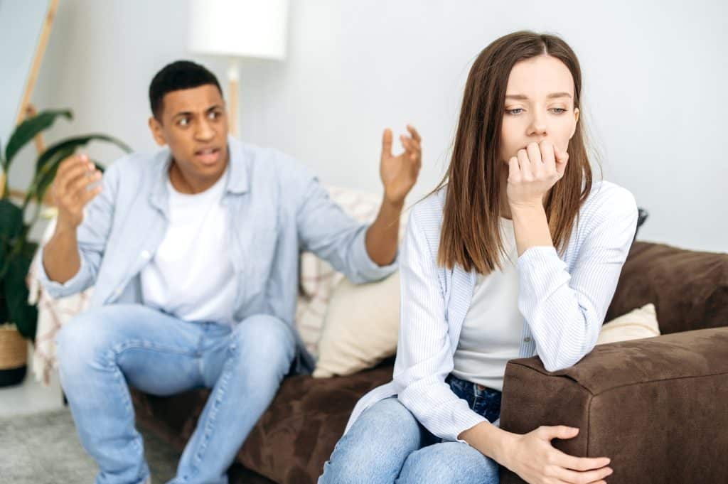Mixed race couple sitting on a sofa in the living room, an angry man yells at a woman, feels angry