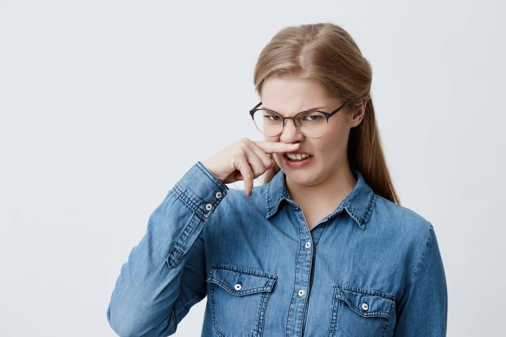 Portrait of a disgusted girl pinching nose. Blonde woman holding nose smelling something stinking