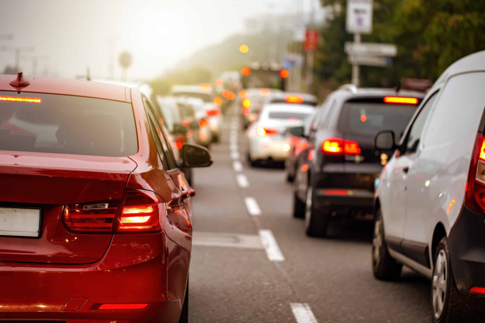 Traffic jam in a city with long queue of cars waiting on a road at sunset