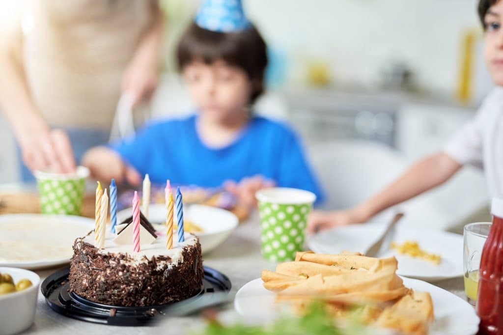 Close up of a birtday cake with candles on the table. Happy hispanic family with kids celebrating