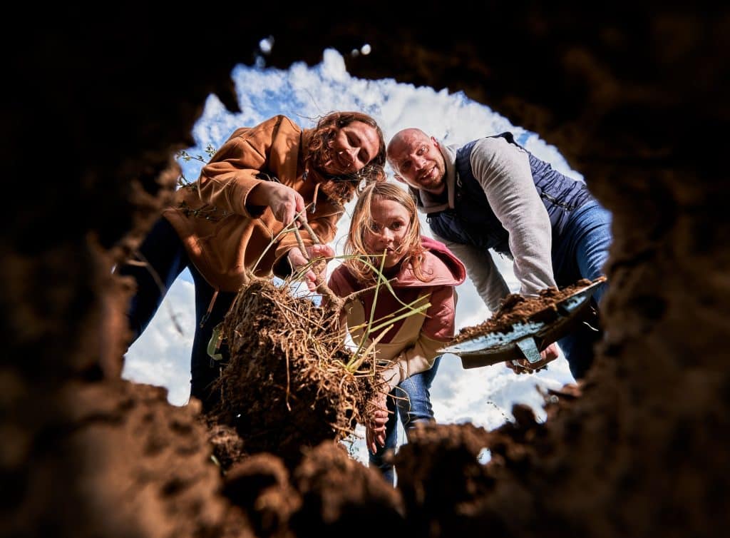 Low view of smiling family looking at hole for planting tree seedling.