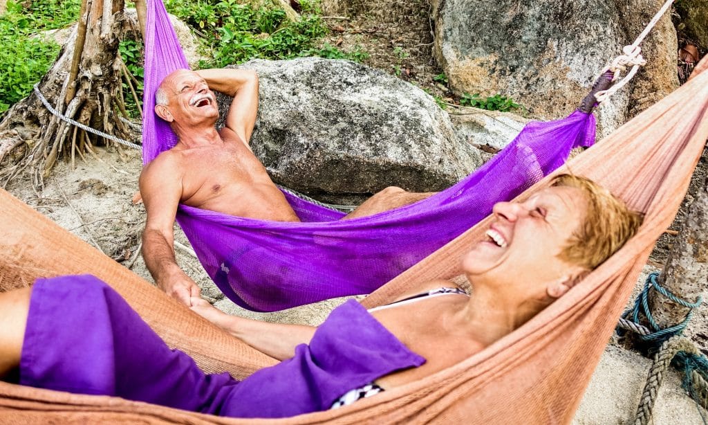 Senior retired couple vacationer relaxing on hammock at beach