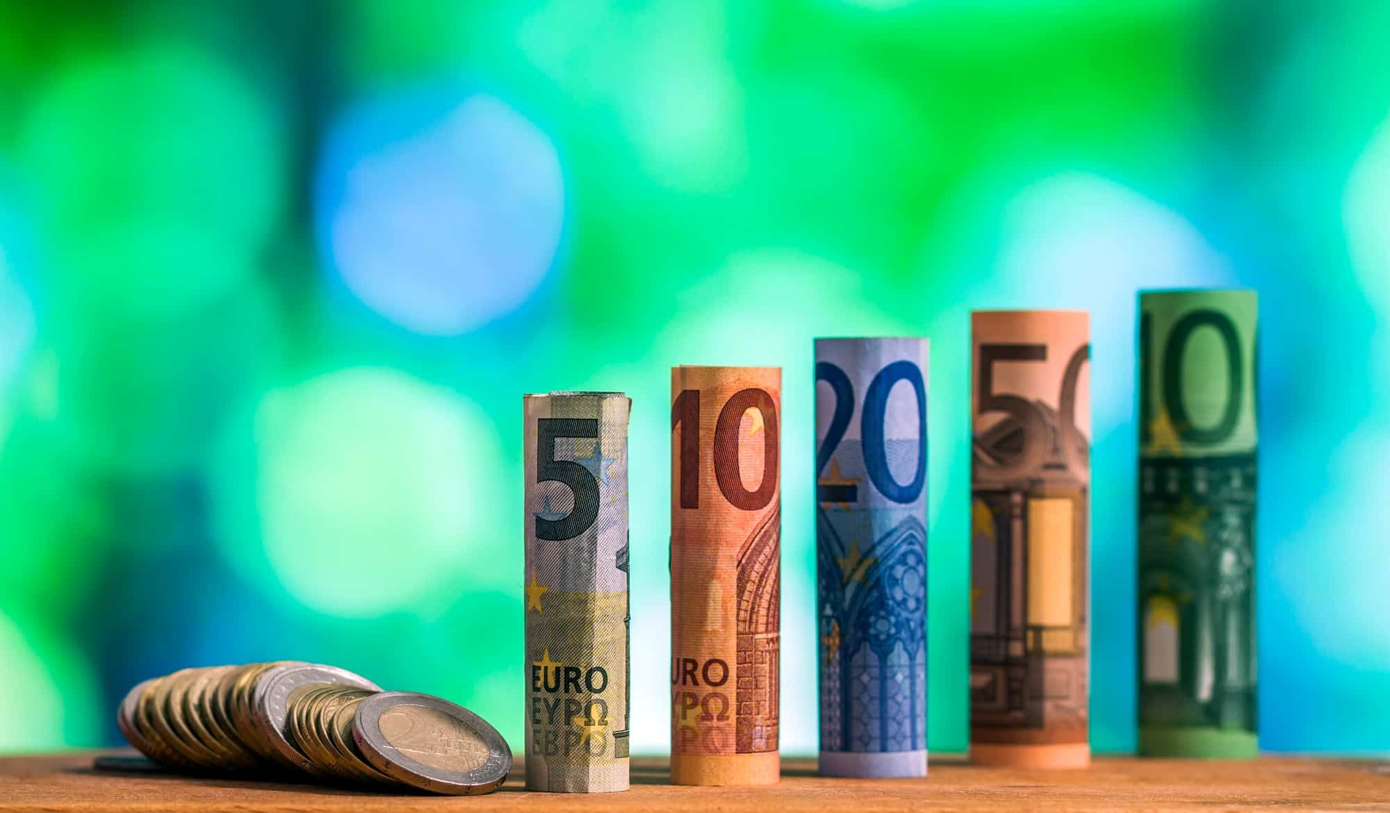Five, ten, twenty, fifty and one hundred euro rolled bills banknotes, with euro coins on green