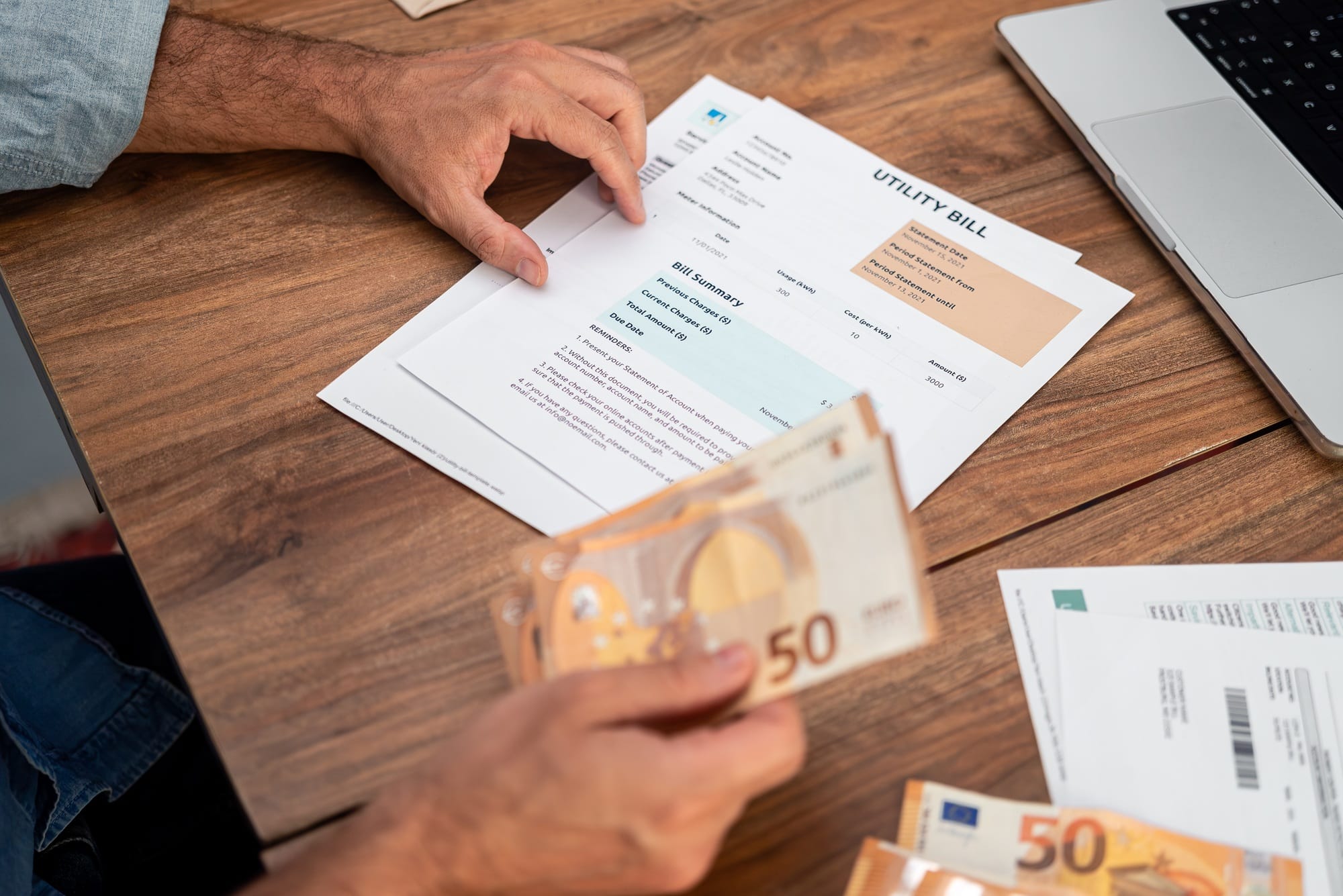 Senior man reads utility bill holding euro banknotes in hand at wooden desk planning budget