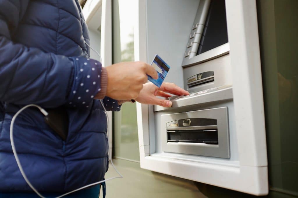 Young woman using cash machine, mid section